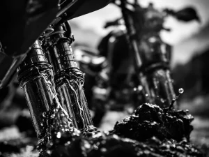 Motorcycle fork tubes with oil dripping down chrome surfaces in dramatic black and white close-up