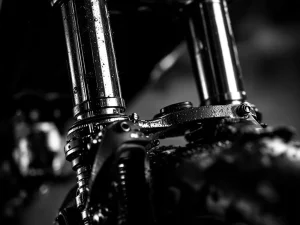 Close-up of motorcycle front fork suspension with chrome stanchion tubes, oil residue, and dust showing friction points
