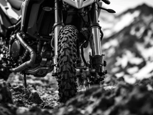 Adventure motorcycle front fork suspension with chrome tubes and triple clamps, knobby tire tread, mountain background