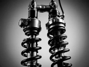 Two motorcycle shock absorbers in black and white: piggyback reservoir on left, remote reservoir with braided hose on right  Note: This response is 124 characters including spaces.
