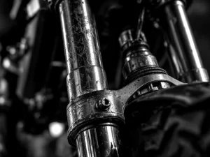 Worn motorcycle fork suspension with scratches, misaligned bushings, and dirt buildup showing mechanical binding issues