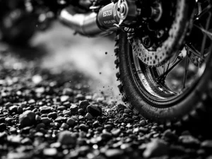 Adventure motorcycle suspension system compressing over rocky terrain in dramatic black and white close-up