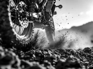 Adventure motorcycle rear suspension compressed mid-action on rocky terrain with dirt particles and dramatic lighting