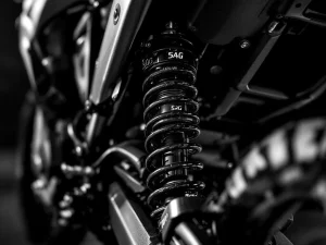 Close-up of adventure motorcycle rear shock absorber with sag measurement indicators and adjustment mechanisms in dramatic lighting