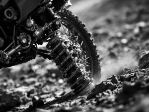 Adventure motorcycle rear suspension at full extension showing shock absorber, linkage, and spring coils in off-road terrain