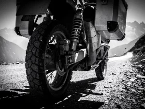 Rear suspension and shock absorber of a loaded adventure motorcycle compressed under panniers on a misty gravel mountain pass.