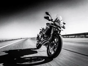 CFMOTO 450 MT adventure motorcycle leaning through a sweeping highway curve, low-angle monochrome shot with motion blur and sharp suspension detail.