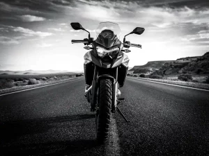 CFMOTO 450 MT adventure motorcycle on an empty highway stretching to the horizon, low-angle cinematic monochrome shot against vast wilderness sky.