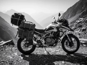 CFMOTO 450 MT adventure motorcycle loaded with saddlebags and tail bag on a rocky mountain trail, misty peaks in the background.