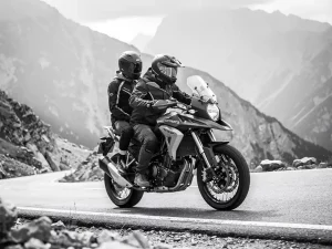 CFMOTO 450 MT adventure motorcycle with two riders navigating a winding mountain road, dramatic grayscale contrast against a misty backdrop.