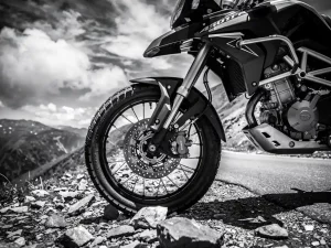 CFMOTO 450 MT adventure motorcycle front fork and handlebars shot from low angle on rocky mountain road, dramatic black and white.