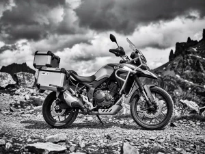 CFMOTO 450 MT adventure motorcycle with panniers and top case parked on a gravel mountain trail, dramatic black and white photography.