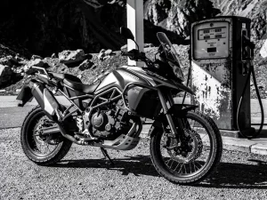 CFMOTO 450 MT adventure motorcycle with knobby tires parked at a remote mountain gas station, dramatic black and white side lighting.