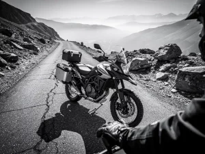 CFMOTO 450 MT adventure motorcycle with saddlebags on a misty mountain road, gloved hand on handlebar, rocky highland valley in background.