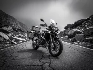 CFMOTO 450 MT adventure motorcycle with saddlebags on a remote mountain road, winding into misty highland terrain, black and white cinematic shot.
