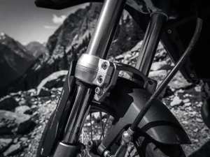 CFMOTO 450 MT adventure motorcycle front fork suspension with chrome stanchions and axle clamps, mountain trail in background, dramatic black and white.