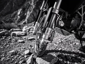 CFMOTO 450 MT front fork suspension with chrome stanchions and dust seals, shot from low angle on a rocky gravel trail.