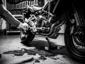 Mechanic's gloved hand gripping a wrench on the suspension linkage of a CFMOTO 450 MT adventure motorcycle in a workshop.