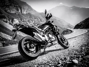 CFMOTO 450 MT adventure motorcycle leaning into a mountain switchback on a gravel road, black and white cinematic shot highlighting suspension detail.