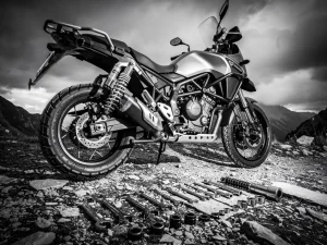 CFMOTO 450 MT adventure motorcycle on mountain trail with aftermarket rear shock absorber, suspension tools on rocky ground, dramatic overcast sky.