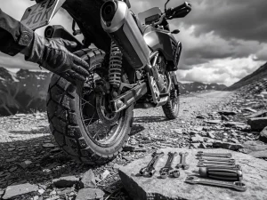 CFMOTO 450 MT adventure motorcycle rear suspension inspected by mechanic on mountain trail, tools on rock, dramatic monochrome light.