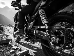 CFMOTO 450 MT adventure motorcycle rear shock absorber compressed under dual-rider weight on a rocky mountain trail, black and white.