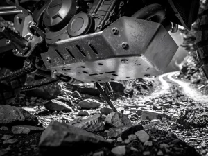 Steel skid plate on a CFMOTO 450 MT adventure motorcycle protecting the undercarriage over rocky, muddy trail terrain.