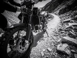 CFMOTO 450 MT adventure motorcycle suspension fork and rear shock absorber on rocky mountain trail, black and white close-up.