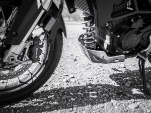CFMOTO 450 MT front fork showing compression and misalignment wear, with rear shock absorber detail on gravel road in dramatic monochrome lighting.