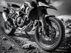 CFMOTO 450 MT adventure motorcycle on gravel trail, front fork compressed and rear shock absorber visible, rugged suspension detail in monochrome.