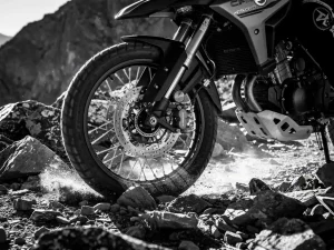 CFMOTO 450 MT adventure motorcycle suspension fully compressed over jagged rocky trail, low-angle monochrome shot highlighting fork tubes and rear linkage articulation.