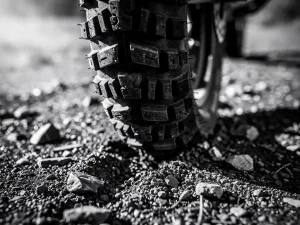 Close-up of a CFMOTO 450 MT adventure motorcycle tire pressing into wet gravel, showing aggressive knobby tread in black and white.