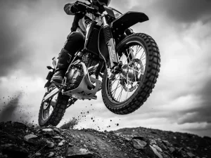 CFMOTO Ibex 450 airborne over rugged terrain, aftermarket coilover suspension visible on front fork, gravel and dust frozen mid-flight beneath wheels.