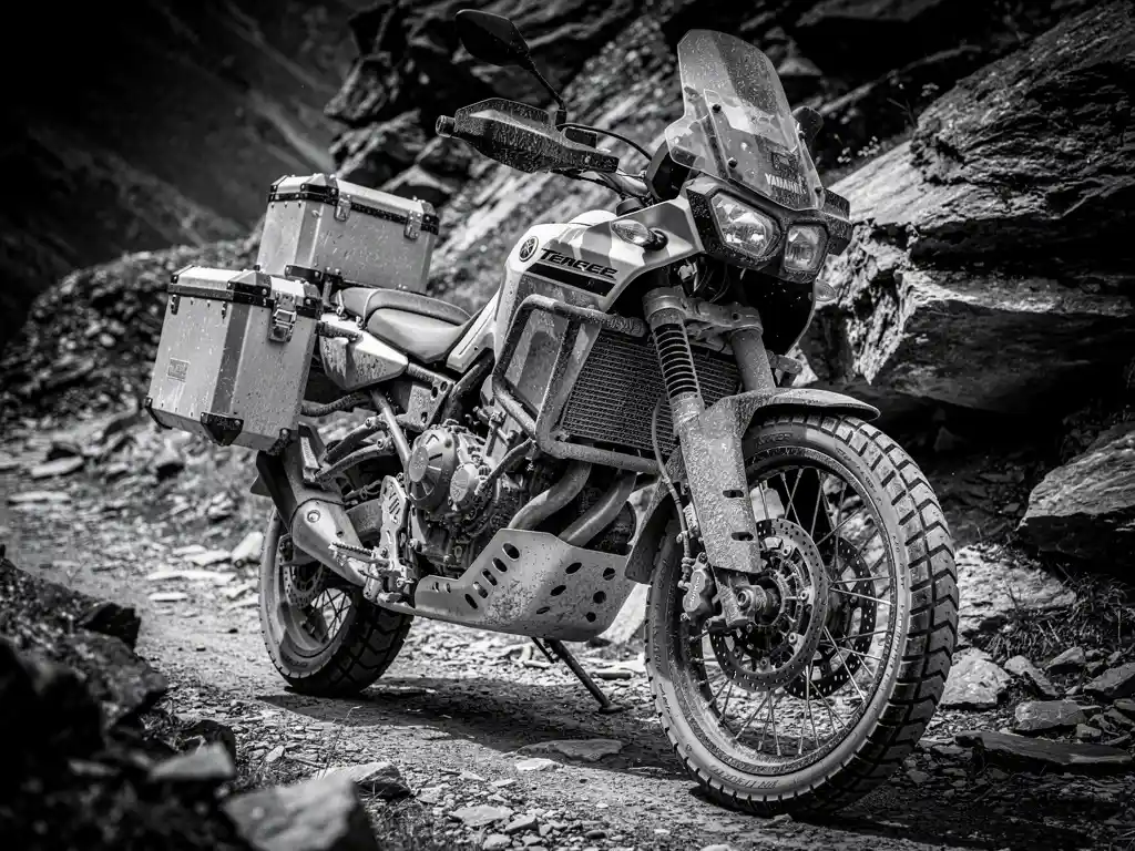 Yamaha Ténéré 700 adventure motorcycle with panniers, handlebar guards, and skid plate parked on rocky mountain trail, dramatic black and white close-up.